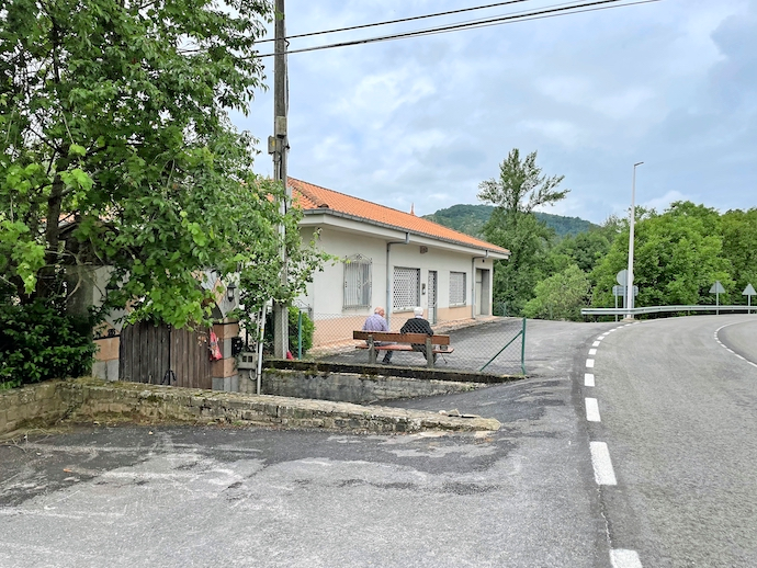 Dos personas de avanzada edad frente al consultorio m&eacute;dico de Anievas, al otro lado de la carretera. / ALERTA