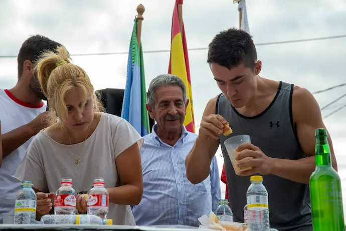 El presidente de Cantabria, Miguel &Aacute;ngel Revilla, mira entusiasmado como engullen sobaos los concursantes el 27 de julio de 2022. / ALERTA