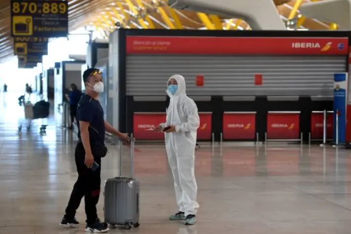 Un pasajero ataviado con un traje de protecci&oacute;n espera junto a un familiar tras facturar un vuelo con destino a Pek&iacute;n en el aeropuerto de Barajas. / E.P.