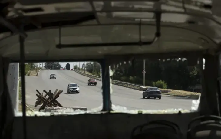 Autom&oacute;viles pasan junto a un autob&uacute;s destruido a un costado de la carretera que conduce a Dnipro (Ucrania). EFE / Orlando Barr&iacute;a
