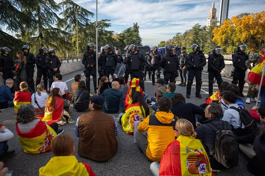 nos j&oacute;venes con banderas y pancartas protagonizan una sentada frente a efectivos de la Polic&iacute;a Nacional durante la manifestaci&oacute;n que han trasladado hasta las inmediaciones de La Moncloa y los accesos de la A-6 a la capital. EFE / Daniel Gonz&aacute;lez