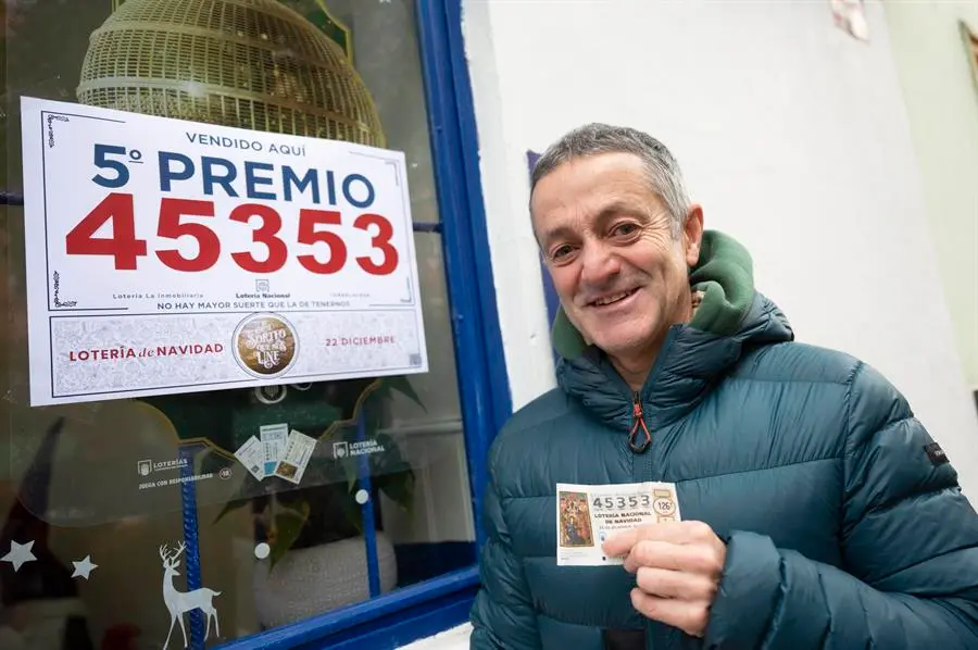 TORRELAVEGA, 22/12/2023.- Un agraciado con un d&eacute;cimo del n&uacute;mero 45.353, uno de los quintos premios del sorteo extraordinario de la Loter&iacute;a de Navidad, posa ante la administraci&oacute;n n&ordm; 6 de Torrelavega este viernes. EFE/ Pedro Puente Hoyos
