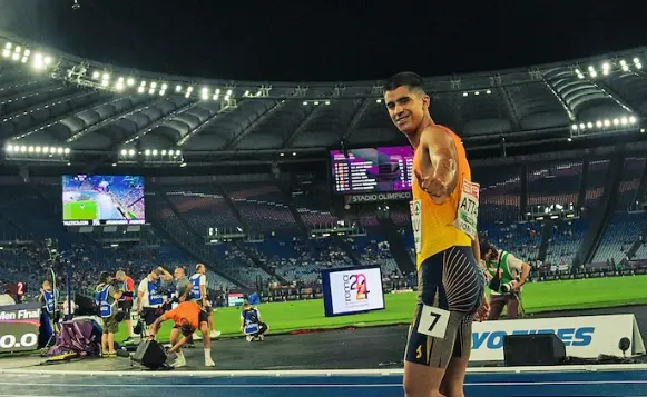 El atleta sonr&iacute;e y saluda tras completar una carrera en el estadio, mostrando su satisfacci&oacute;n y optimismo durante la competici&oacute;n nocturna.