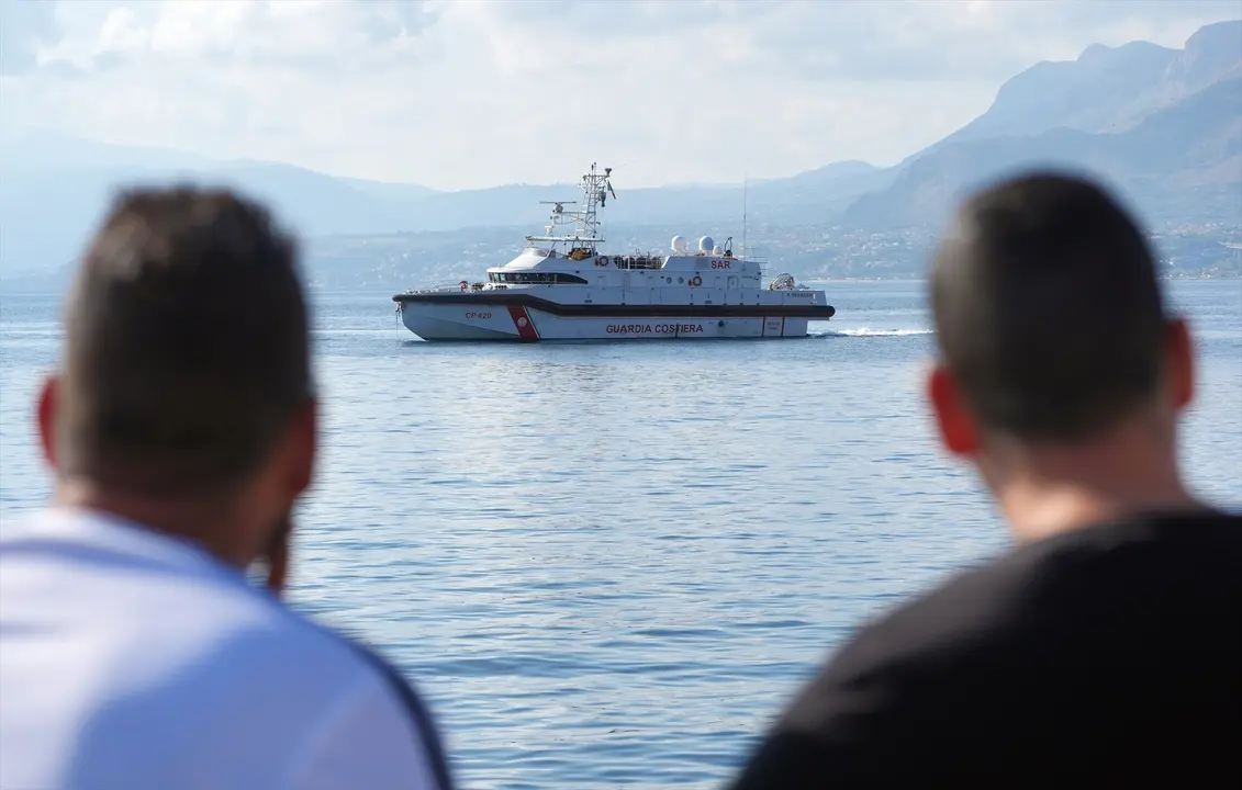 Dos personas miran el barco de la Guardia Costera que trabaja en las labores de rescate. Jonathan Brady
