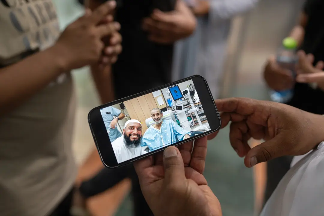 El reh&eacute;n israel&iacute; liberado Kaid Alkadi fotografiado en el interior de la sala de urgencias con un tel&eacute;fono m&oacute;vil mientras sus familiares se re&uacute;nen frente al Centro M&eacute;dico de Beersheva, en el sur de Israel. / Ilia yefimovich
