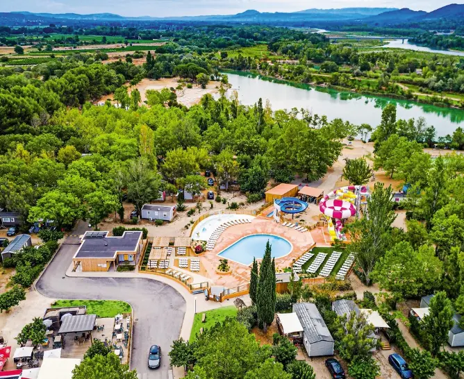 Vista a&eacute;rea de un camping 4 estrellas rodeado de naturaleza, con piscina, zonas recreativas y acceso directo a un r&iacute;o, ideal para unas vacaciones de relax y diversi&oacute;n al aire libre.