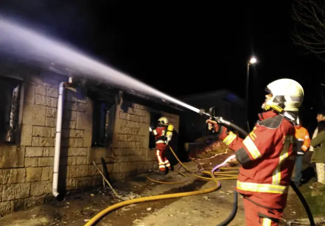 Un efectivo trabaja para sofocar las llamas en la caba&ntilde;a afectada en San Pedro del Romeral, mientras el fuego deja severos da&ntilde;os en la fachada y la cubierta del inmueble.