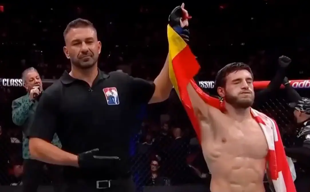 Aleksandre Topuria celebra su victoria en su debut en la UFC, con el &aacute;rbitro levantando su brazo en se&ntilde;al de triunfo. Envuelto en la bandera de Espa&ntilde;a y Georgia, el hispano-georgiano se impone por decisi&oacute;n un&aacute;nime en UFC 312, marcando el inicio de su camino en la &eacute;lite de las artes marciales mixtas.