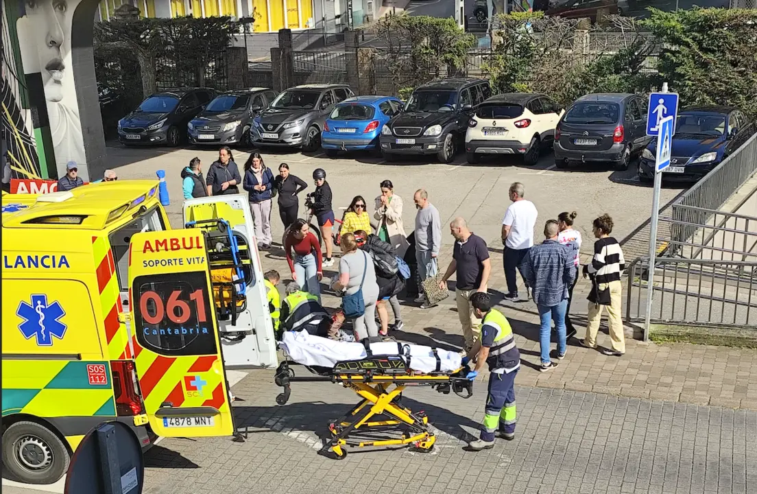 Los servicios de emergencias atienden a la v&iacute;ctima tras un brutal apu&ntilde;alamiento en plena v&iacute;a p&uacute;blica, mientras los testigos observan con preocupaci&oacute;n. La ambulancia del 061 de Cantabria se encuentra en el lugar para trasladar al herido con urgencia.