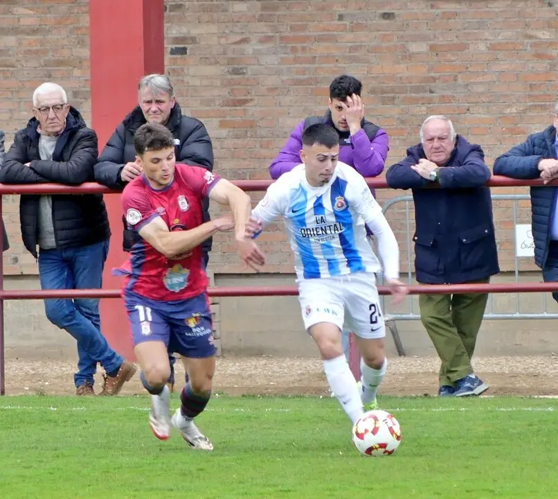 El jugador de la Gimn&aacute;stica intenta avanzar por la banda ante la presi&oacute;n de un rival del Real &Aacute;vila, en una acci&oacute;n del encuentro disputado en el Estadio Adolfo Su&aacute;rez, seguido de cerca por el p&uacute;blico desde la barandilla.