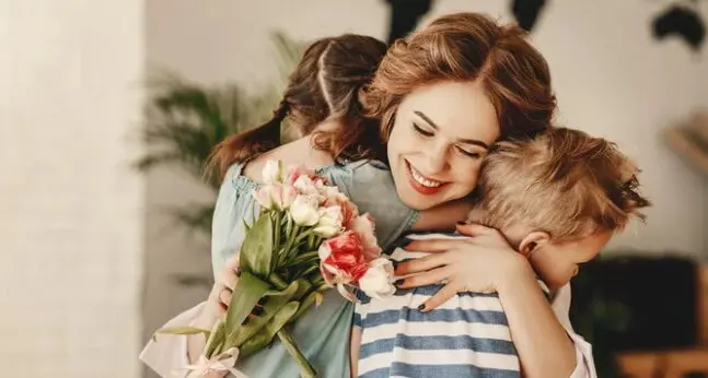 Una madre abraza a sus hijos tras entregarle un ramo de flores. / A.S.