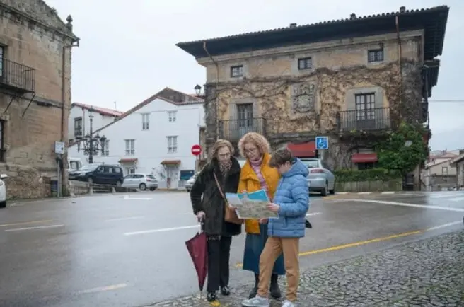 Tres visitantes consultan un mapa en el centro hist&oacute;rico de Santillana del Mar durante una jornada gris y h&uacute;meda en Cantabria.