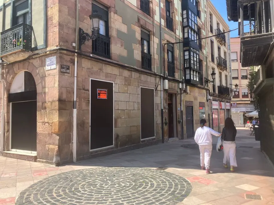 Dos personas paseando por una calle de Torrelavega con un local de grandes dimensiones vac&iacute;o. / S.D.