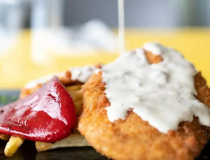 Salsa de queso cabrales sobre pechugas de pollo crujientes con patatas fritas, pimientos asados. / La Corbata