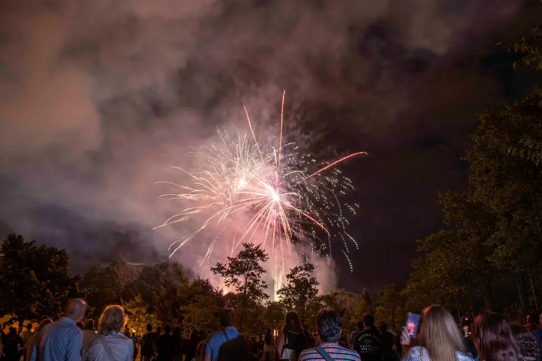 Espectadores contemplan el espect&aacute;culo de fuegos artificiales en una noche de celebraci&oacute;n bajo un cielo cubierto de humo y nubes.