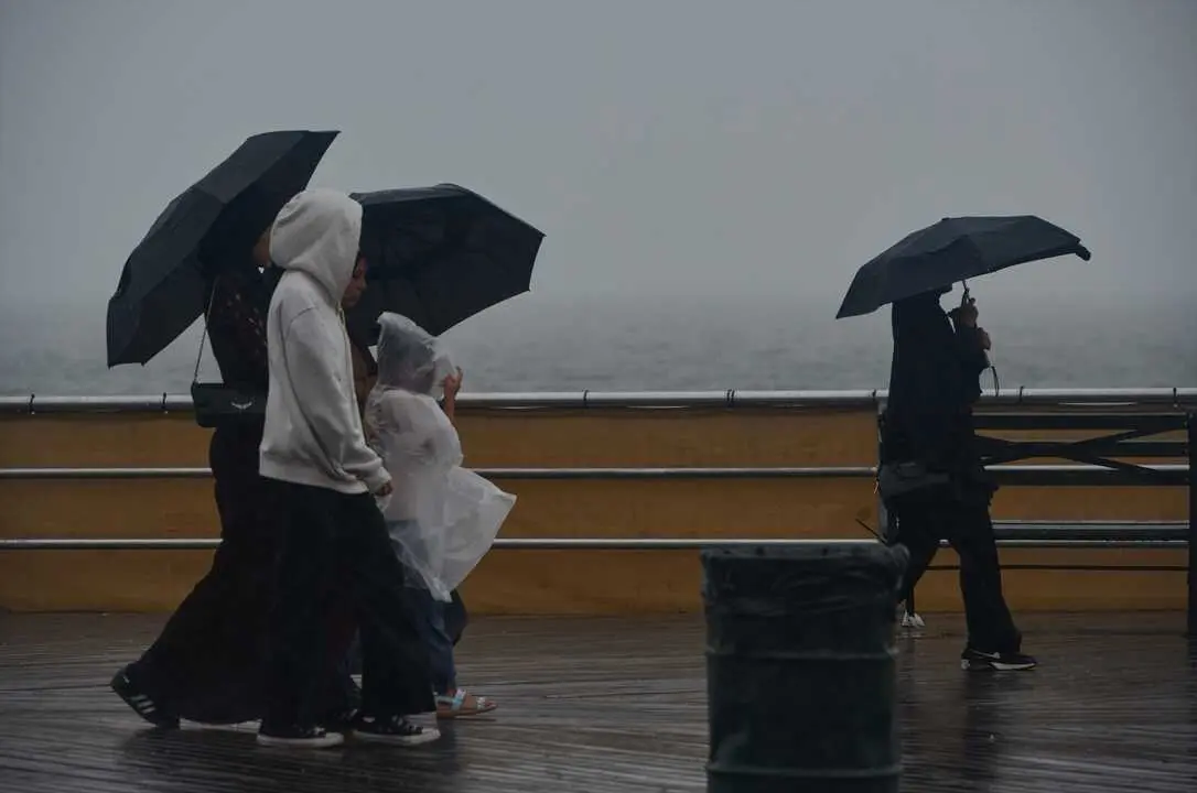 Varias personas pasean bajo la lluvia al lado de la playa. / Edna Leshowitz