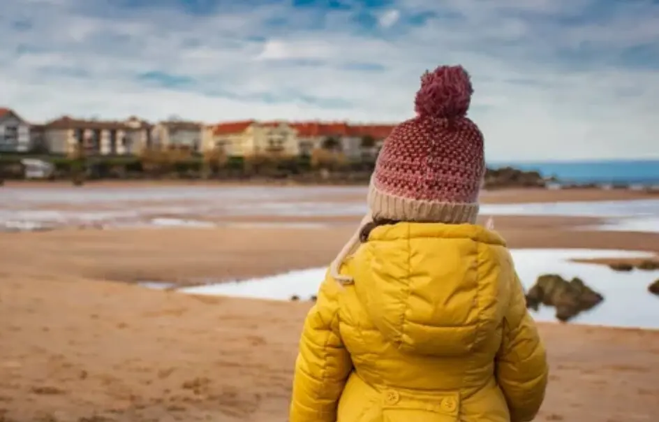 Una ni&ntilde;a observa la playa en Cantabria en una jornada de cielos cubiertos y temperaturas suaves, t&iacute;pica del invierno.