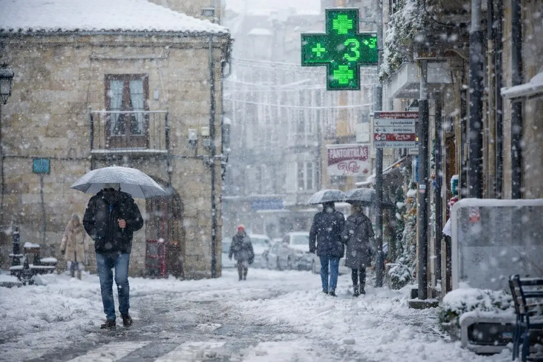 Varias personas caminan por Reinosa bajo la nevada. / AI