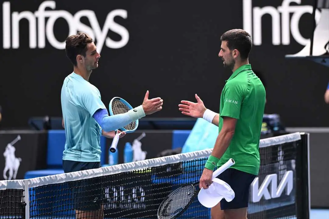 Novak Djokovic saluda en la red a Lorenzo Mussetti tras el abandono del italiano en los cuartos de final del Abierto de Australia 2026. / Joel Carrett