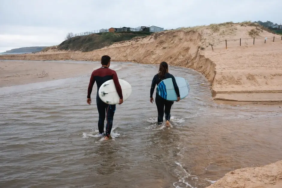 Dos surfistas avanzan por el agua rumbo al mar en una ma&ntilde;ana gris, buscando las primeras olas del d&iacute;a.