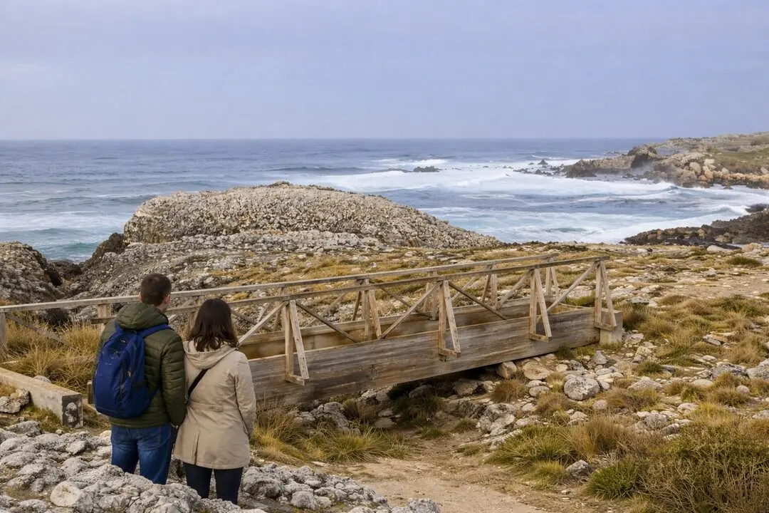 Dos curiosos observan el oleaje desde la izquierda del puente, contemplando la fuerza del mar en la costa rocosa.