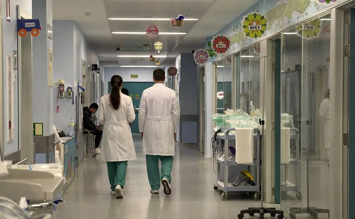 Dos profesionales sanitarios recorren uno de los pasillos hospitalarios de Cantabria en plena escalada de la huelga m&eacute;dica, marcada por la tensi&oacute;n asistencial y el enfrentamiento entre administraciones y sindicatos.