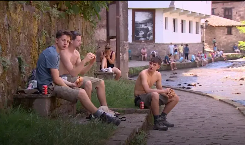 Varias personas descansan junto al r&iacute;o en Potes para combatir las altas temperaturas durante la jornada de alerta roja por calor en la comarca de Li&eacute;bana.