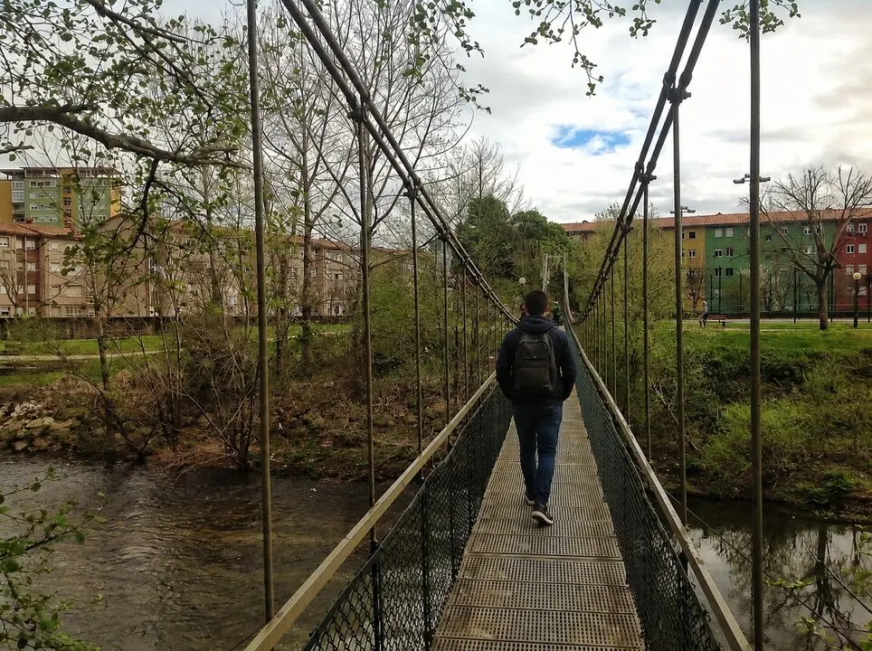 Una persona cruza el puente colgante del parque de La Viesca, una de las infraestructuras peatonales m&aacute;s emblem&aacute;ticas de este espacio natural situado entre Torrelavega y Cartes, muy frecuentado por senderistas, ciclistas y paseantes.