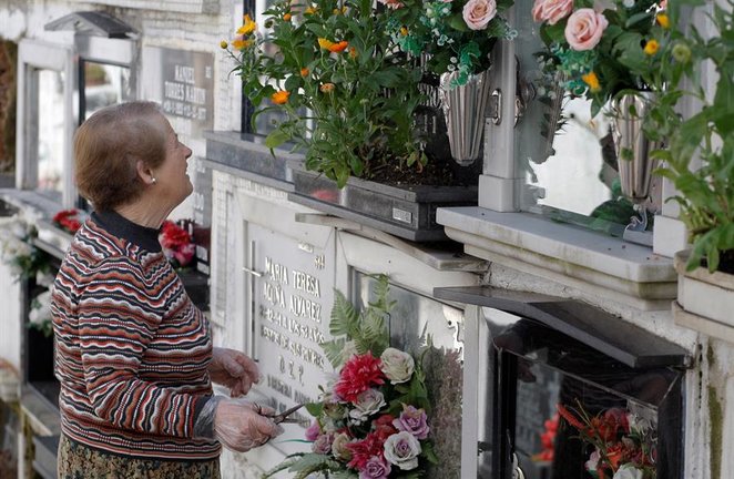 Una mujer arregla ofrendas florales en la tumba de un familiar en el cementerio. /Juan González