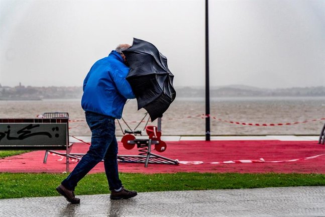 Un hombre sujeta con fuerza su paraguas mientras camina este lunes por la bahía de Santander. Cantabria permanece en alerta por fuertes vientos y oleaje debido a la borrasca "Bella". EFE/Román G. Aguilera