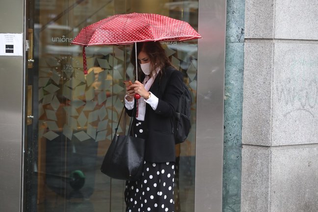 Archivo - Una mujer protegida con un paraguas camina por el centro de la capital,.