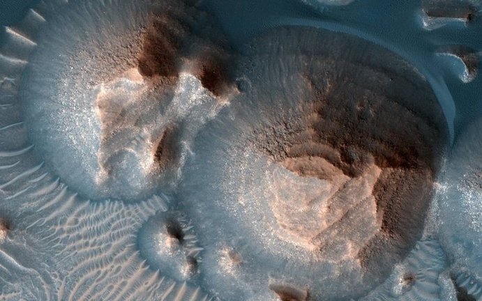 Esta imagen muestra varios cráteres en Arabia Terra que están llenos de capas de roca, a menudo expuestos en montículos redondeados.