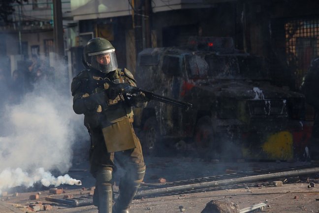 Archivo - Un agente de Carabineros con una escopeta antidisturbios en medio de gases lacrimógenos durante una protesta en Concepción en noviembre de 2019