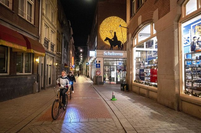 Personas montando en bicicleta junto a tiendas cerradas en Ámsterdam, Países Bajos, el 28 de noviembre de 2021. La hora de cierre de todos los locales y eventos es entre las 17:00 y las 5:00 horas. (Países Bajos; Holanda) EFE/EPA/Evert Elzinga