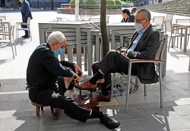 Un persona limpia los zapatos de otro en la plaza de la Catedral de Santander. / J. Ramón