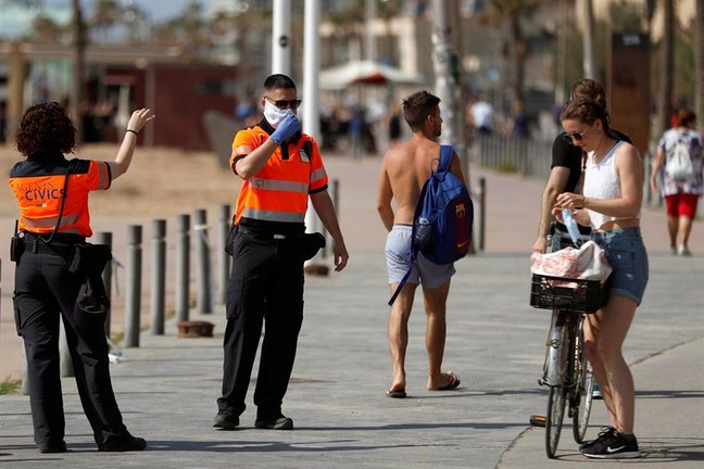 Agentes Civicos indican a una joven que se coloque la mascarilla protectora, este sábado en el paseo marítimo de la Barceloneta en Barcelona. EFE/Toni Albir