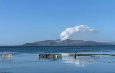 Un hombre camina por las aguas del lago Taal mientras las cenizas y el vapor se elevan desde el cráter del volcán Taal. - Girlie Linao / dpa - Archivo