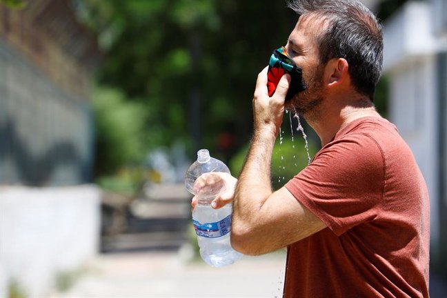 Un hombre refresca su mascarilla ante las altas temperaturas. / EFE