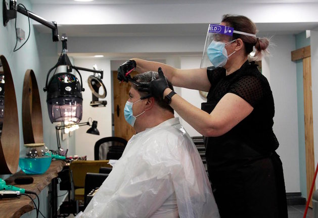 Una persona con mascarilla le corta el pelo en una peluquería de Santander. / J.R.