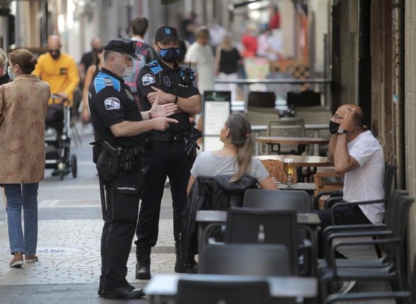 Dos agentes de la policía se dirigen a un hombre que se encontraba fumando en una terraza de un bar de la ciudad. EFE/ CABALAR