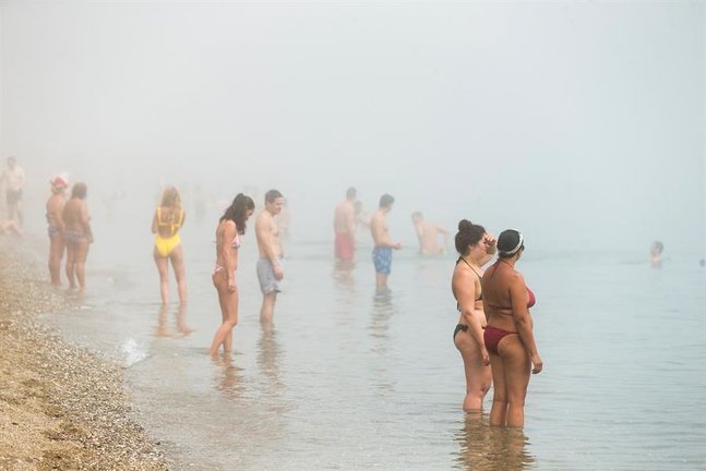 Numerosas personas disfrutan en la playa de la Malageta entre un banco de taró, la niebla que entra desde el mar, y que ha sido visible en todo el cielo de Málaga por segundo día consecutivo.EFE/ Jorge Zapata