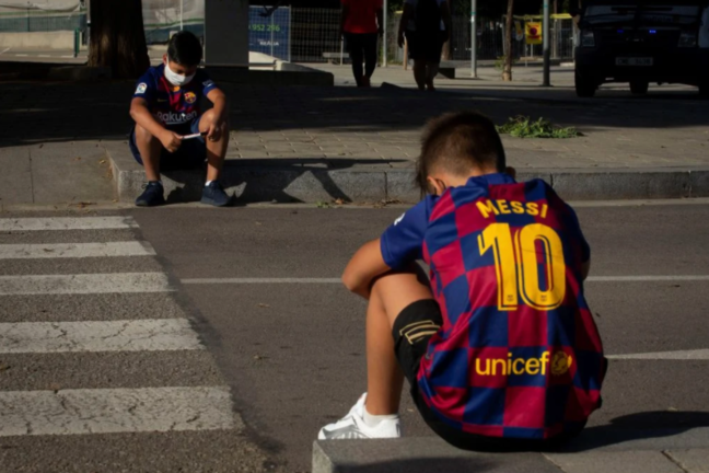 Dos chicos esperan a la entrada de la ciudad deportiva Joan Gamper en Barcelona la llegada de los jugadores. Foto: EFE | Enric Fontcuberta