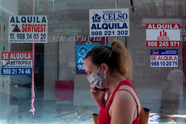 Una mujer con mascarilla pasa ante un comercio cerrado con varios carteles que anuncian su alquiler. EFE/Brais Lorenzo/Archivo