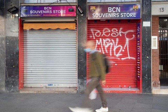 Un vecino pasa ante una tienda de recuerdos con la persiana bajada en un comercio cercano al Camp Nou. EFE/ Marta Pérez/Archivo