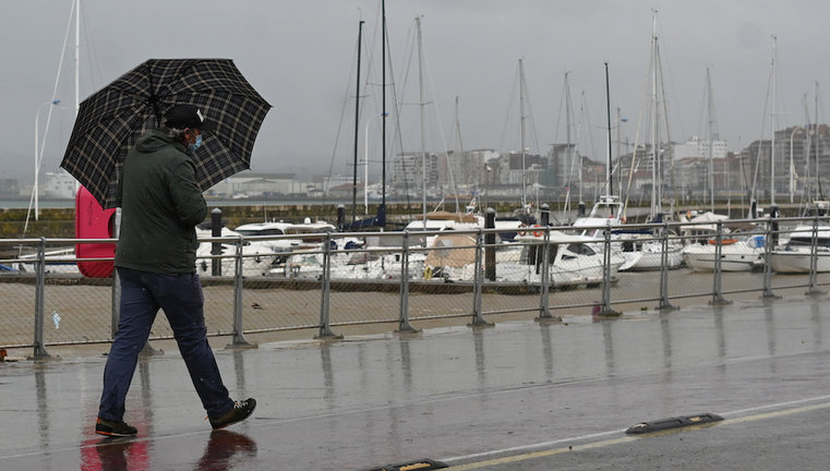 Un hombre camina bajo la lluvia en las inmediaciones de Puertochico en Santander. / HARDY