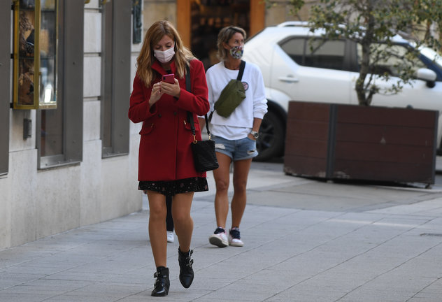 Una persona con su mascarilla observa su teléfono móvil en una calle del centro de Santander. / HARDY