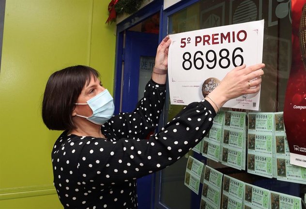 La propietaria de la administración de lotería 81 de Zaragoza coloca el cartel tras haber vendido décimos del número 86986 uno de los quintos premios del Sorteo Extraordinario de Lotería de Navidad, este martes. EFE/Javier Cebollada