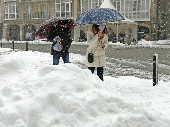 Dos personas caminan con su paraguas bajo la nieve en la localidad de Reinosa. / QUEIMADELOS