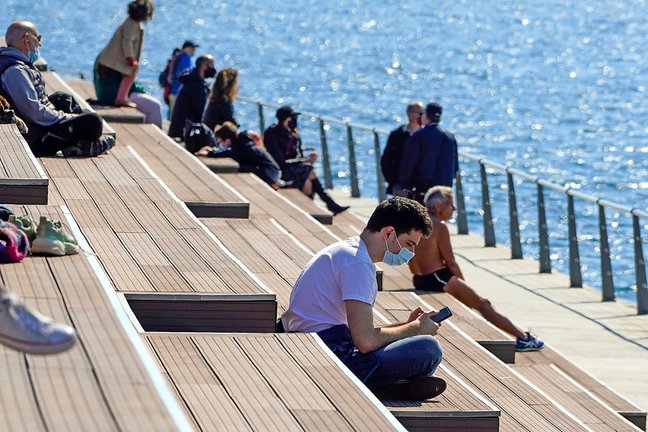Un joven mira su móvil mientras disfruta de un día primaveral ayer domingo en el dique de Gamazo, en Santander. / HARDY