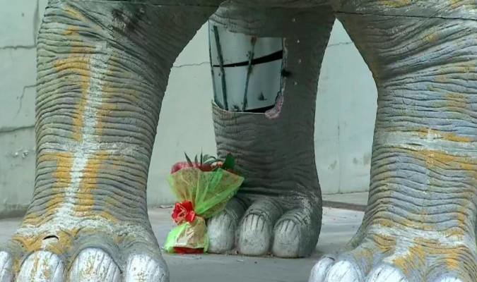 Figura del dinosaurio y de un ramo de flores depositado a los pies. / EFE
